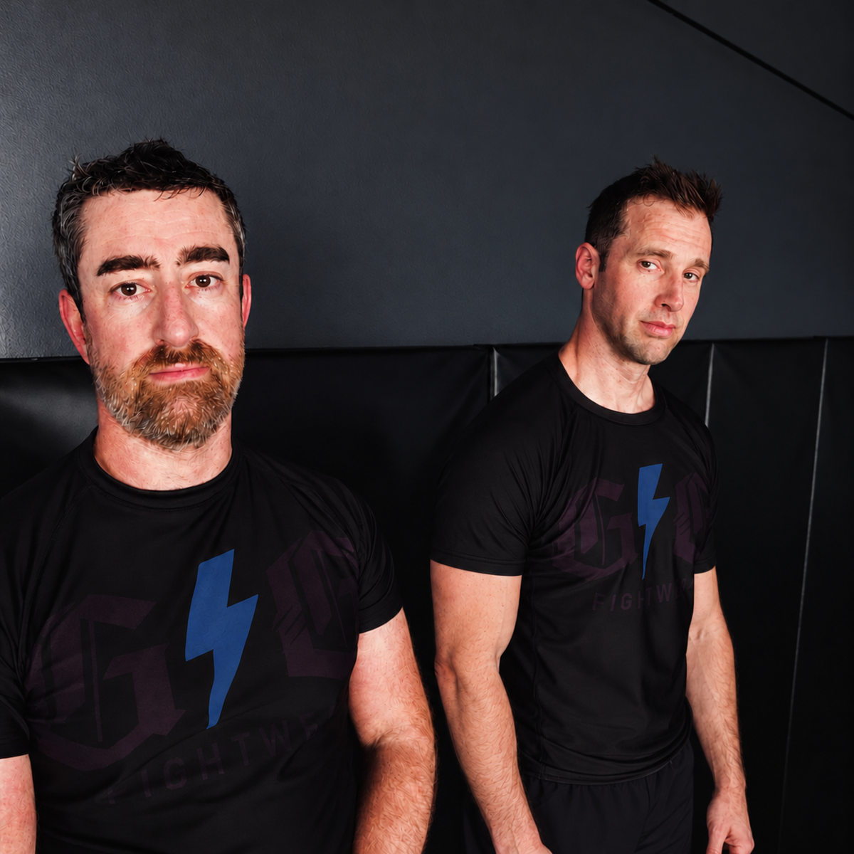 Two grapplers wearing black short sleeve Grip ’N Guard rashguards with blue lightning bolts